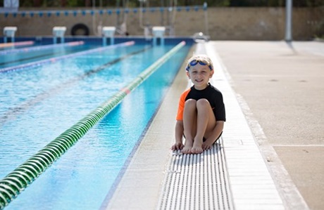 Young boy sitting on the pool edge looking unsure about getting in