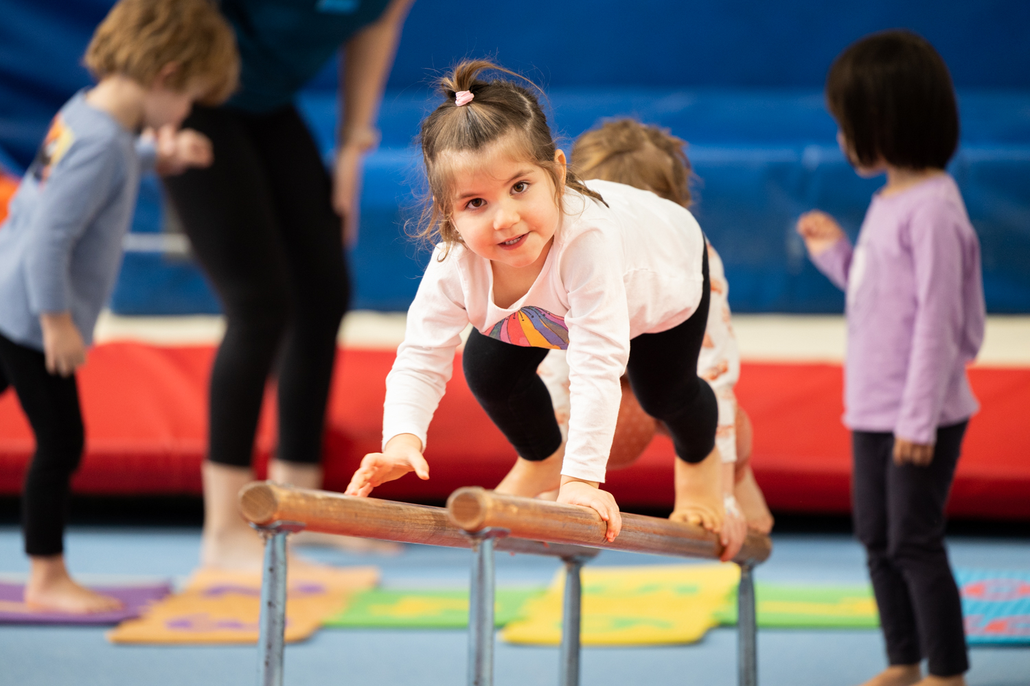 Young girl climbing along parallel bars at kids gymnastics